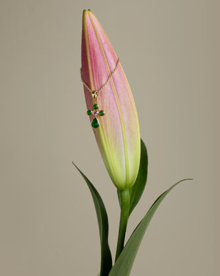 Cross Necklace with green stones displayed on a pink tulip bud against a beige background