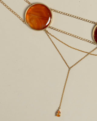 Detail picture of gold choker with amber-colored stones on a beige background