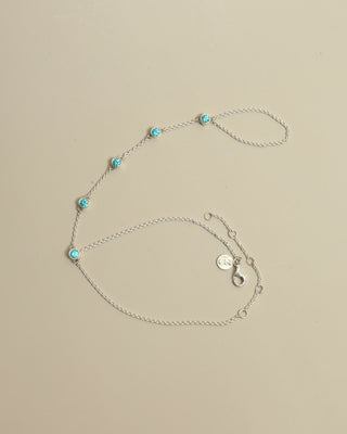 Silver hand chain with turquoise gems on a beige background