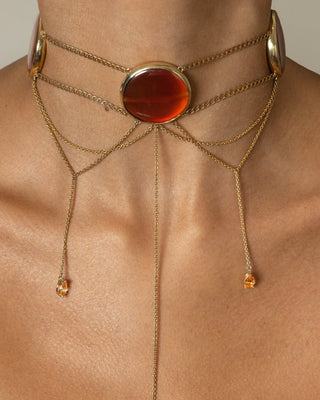 Gold chain necklace with a red/orange agate stone on a models neck against a neutral background