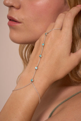 Close-up of the Brisa hand chain across the hand, featuring vibrant bezel-set blue stones.

Primer plano de la cadena de mano Brisa sobre la mano, con piedras azules vibrantes.