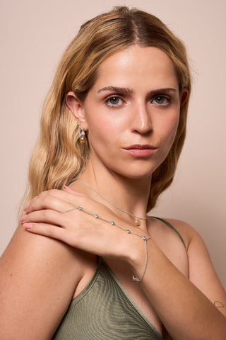 Model showcasing the Brisa hand chain with silver chain and multiple blue gemstones.

Modelo mostrando la cadena de mano Brisa con delicada cadena de plata y varias gemas azules.