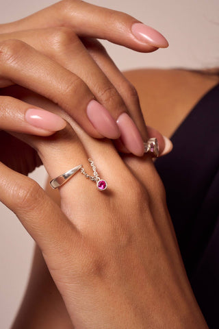Elegant close-up of silver ring with dangling red gemstone on manicured hand.

Primer plano elegante de anillo de plata con gema roja colgante en mano con manicura.
