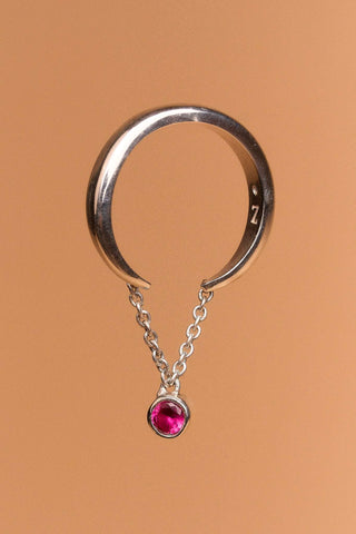Cosma ring in sterling silver with open band and chain, finished with a vivid red stone.

Anillo Cosma en plata esterlina con aro abierto y cadena, terminado con una piedra roja vibrante.