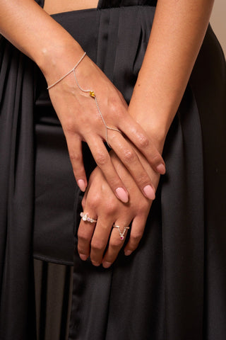 Full view of the Leto hand chain worn with rings, showcasing its delicate silver chain and yellow gem.

Vista completa de la cadena de mano Leto con anillos, mostrando su delicada cadena de plata y gema amarilla.