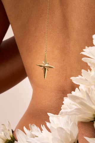 Noema necklace in gold with star pendant styled against bare skin and white flowers.

Collar Noema en oro con dije de estrella, estilizado sobre piel descubierta y flores blancas.
