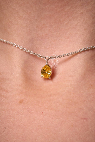 Close-up of the Noema necklace pendant, a brilliant yellow pear-cut stone on a silver chain.

Primer plano del dije del collar Noema, una piedra amarilla corte pera sobre una cadena de plata.