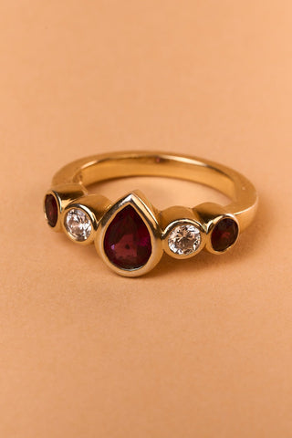 Close-up of the ZOGO Vela Ring in gold vermeil with a deep red pear-cut center stone and bezel-set clear gems.

Primer plano del anillo ZOGO Vela en vermeil de oro con piedra central en corte pera rojo intenso y gemas transparentes engastadas.